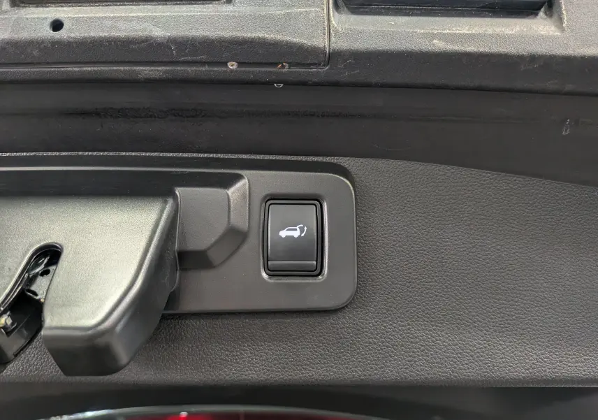 Bouton d'ouverture électrique du coffre sur panneau intérieur noir d'un Renault Symbioz gris Cassiopé, vue rapprochée.