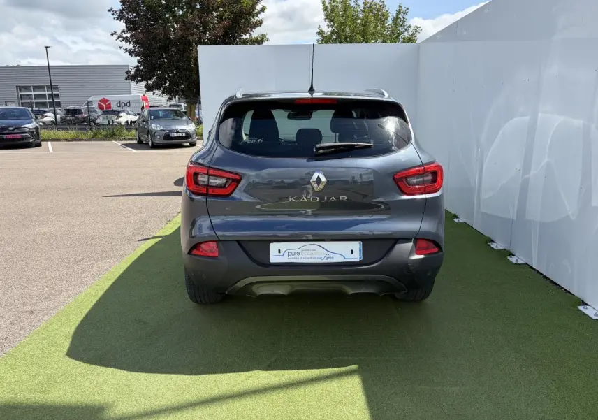 Vue arrière d'un Renault Kadjar bleu métal garé sur sol vert avec feux arrière rouges et logo chromé visible.