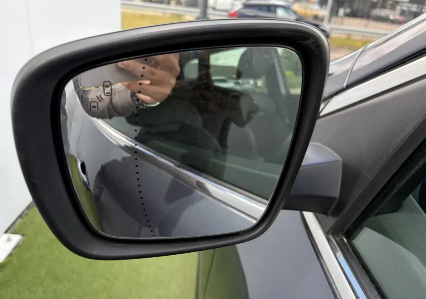 Rétroviseur extérieur côté gauche du Renault Kadjar gris titanium, avec reflet partiel de la portière et du bras du photographe.