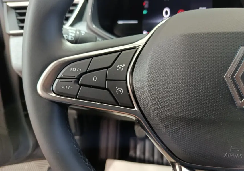 Gros plan sur le volant cuir synthétique gris de la Renault Clio 2025, avec commandes multifonctions et logo central visible.