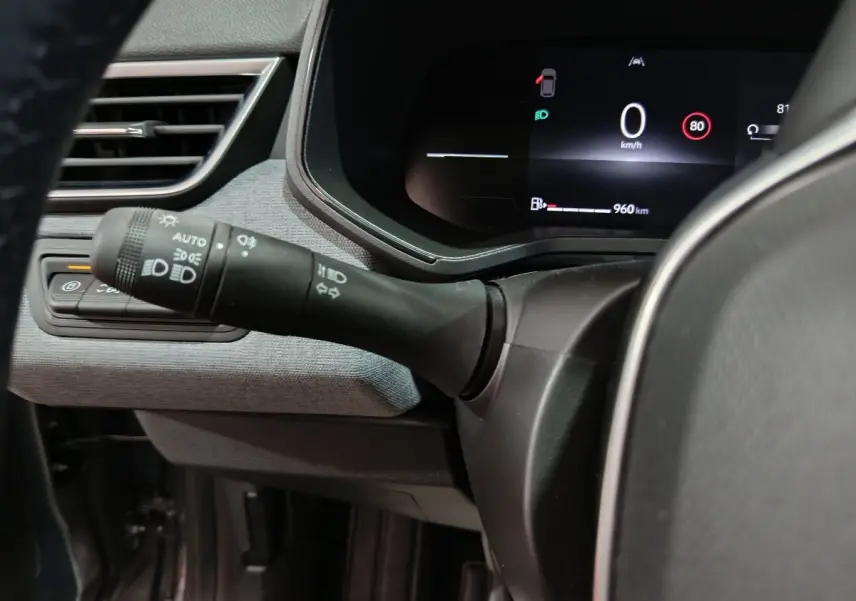 Gros plan intérieur sur la commande des phares et le combiné d'instruments numérique de la Renault Clio gris clair Evolution Blue dCi 100.