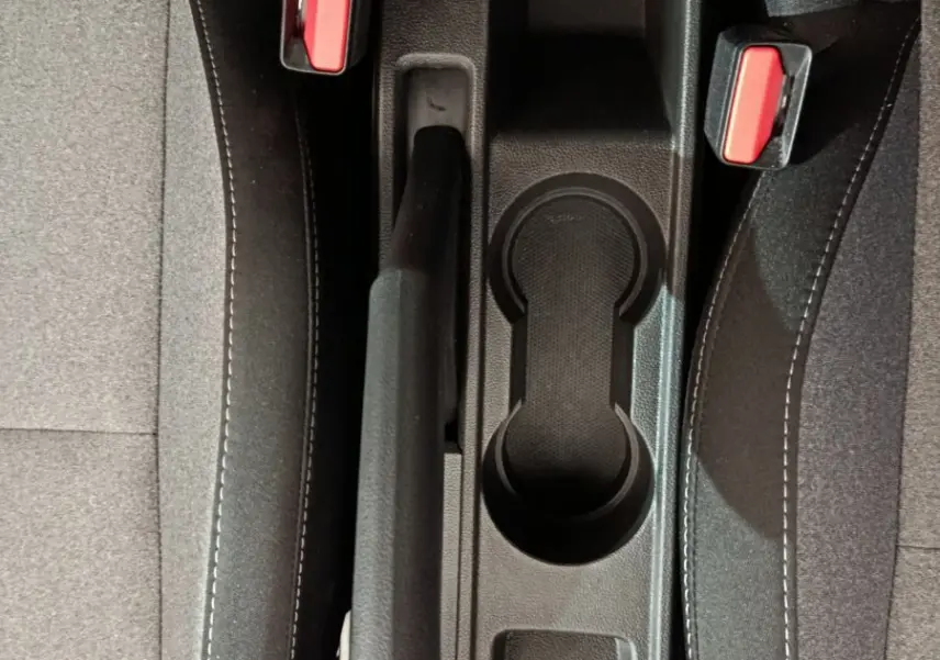 Vue plongeante sur la console centrale noire entre les sièges gris clair de la Renault Clio Evolution 2025, avec frein à main et porte-gobelets.