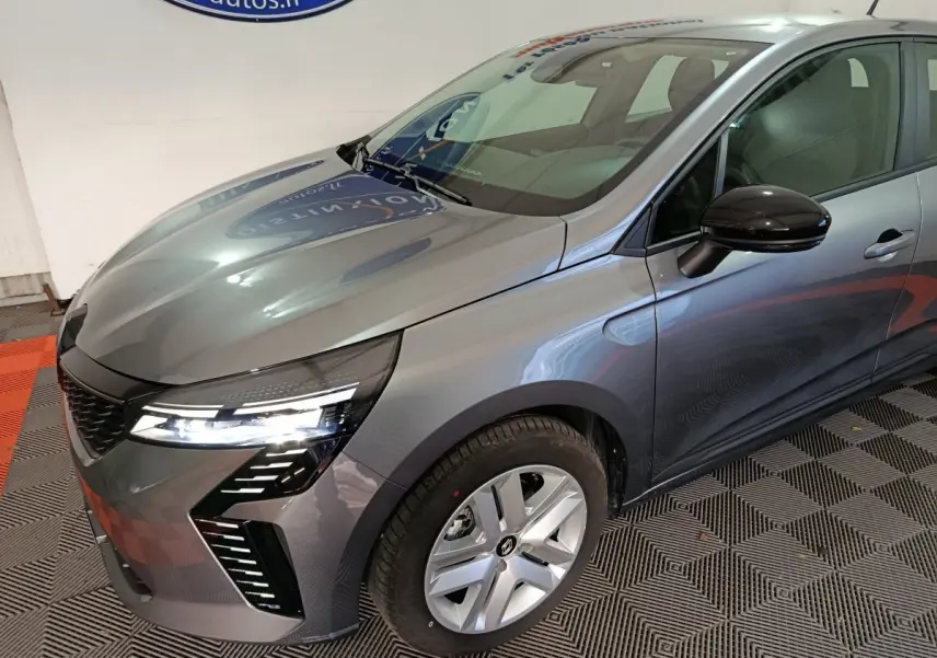 Renault Clio gris clair vue 3/4 avant droit, avec phares LED allumés et rétroviseur noir brillant.