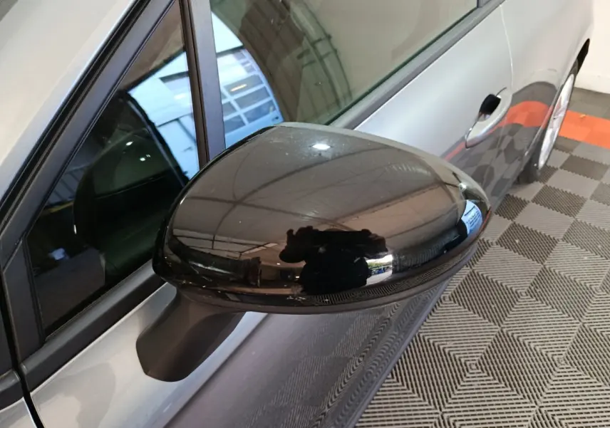 Gros plan sur le rétroviseur noir côté gauche d'une Renault Clio gris clair, vue partielle de la portière avant.