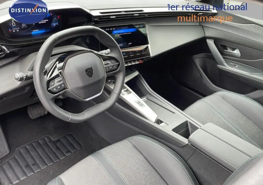 Vue intérieure de la Peugeot 408 2025 montrant le volant, tableau de bord numérique et sièges gris tissu et cuir.
