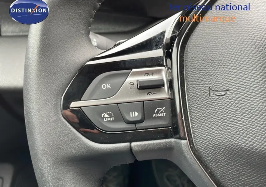 Gros plan sur les commandes à gauche du volant noir du Peugeot 408 1.2 Hybrid 2025, boutons de limitation et assistances visibles.