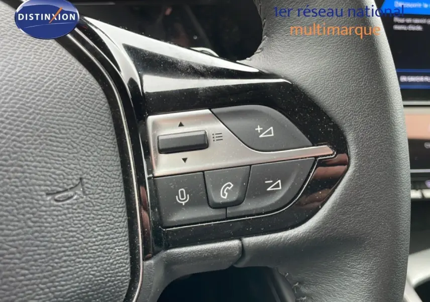 Gros plan sur les commandes multifonctions à gauche du volant cuir noir du Peugeot 408 gris selenium 2025.