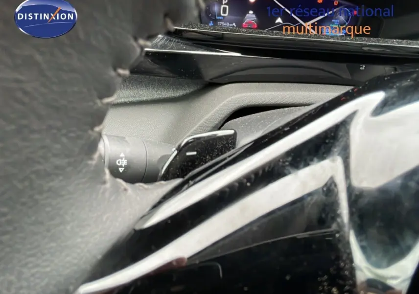 Gros plan sur la palette de changement de vitesses derrière le volant d’une Peugeot 408 gris Selenium, tableau de bord numérique visible.
