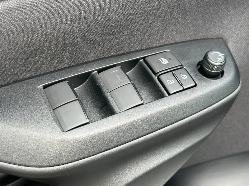 Gros plan sur les commandes de lève-vitres et rétroviseurs côté gauche intérieur de la Toyota Yaris 116h Dynamic 2025 blanc Lunaire.