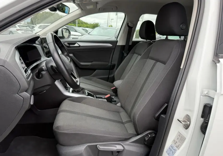 Vue intérieure côté conducteur du Volkswagen T-Roc blanc pur 2022, sièges tissu gris et tableau de bord moderne.