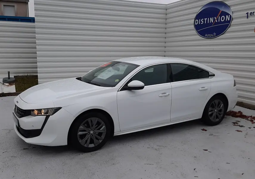 Peugeot 508 blanc vue de profil côté gauche, avec feux avant allumés et jantes foncées, stationnée devant un mur blanc.