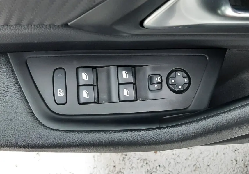 Gros plan sur les commandes de lève-vitres et réglage des rétroviseurs côté conducteur de la Peugeot 508 blanche.