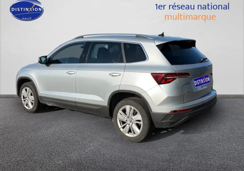 Vue 3/4 arrière droite d'un Skoda Karoq gris avec barres de toit et jantes alliage.