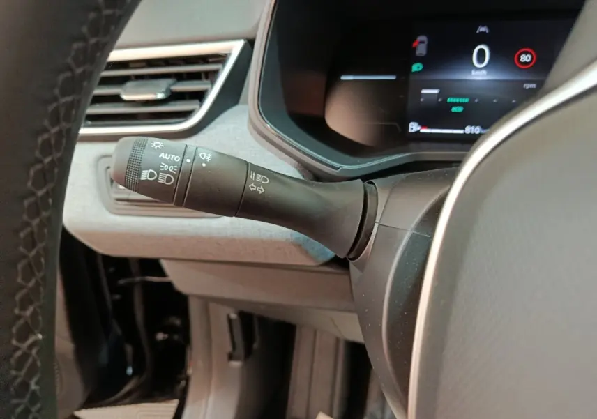 Gros plan intérieur sur la manette de phares et clignotants à gauche du volant d’une Renault Clio noire, tableau de bord numérique visible.