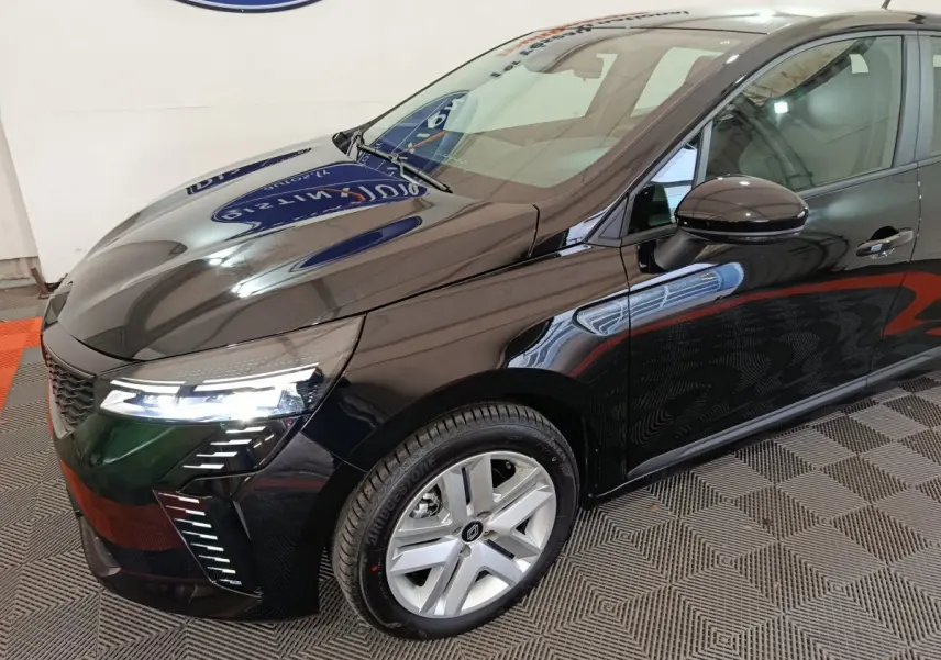 Vue 3/4 avant gauche de la Renault Clio noire 2025 avec phares LED allumés et jantes argentées.