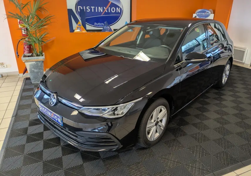 Volkswagen Golf 1.5 eTSI Style noire vue en 3/4 avant droit dans un showroom avec mur orange.