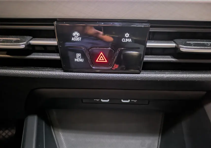 Détail du tableau de bord de la Volkswagen Golf 2024 noir, bouton d'alerte rouge et commandes d'assistance et climatisation.