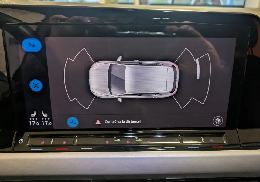 Vue du tableau de bord de la Volkswagen Golf 1.5 eTSI 2024, écran affichant l'aide au stationnement en vue aérienne.
