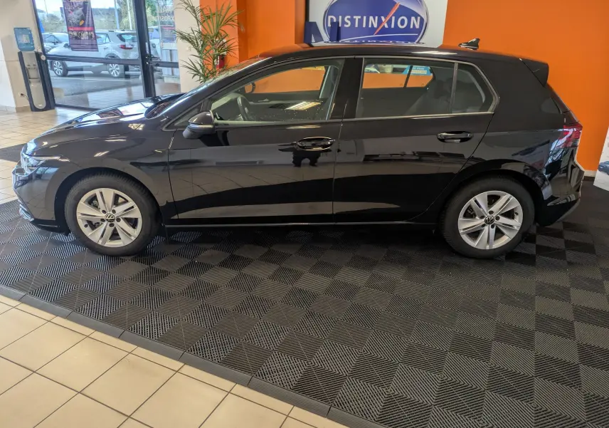 Volkswagen Golf 1.5 eTSI Style noire vue de profil côté gauche en intérieur sur sol damier noir.