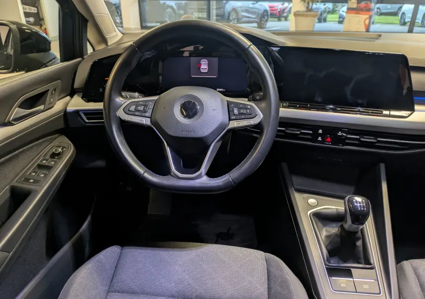 Vue intérieure de face du poste de conduite noir de la Volkswagen Golf 1.5 eTSI 2024 avec volant multifonction et boîte manuelle.