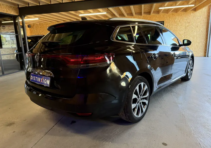 Vue 3/4 arrière droite d'une Renault Mégane Estate noire étoilée 2024, stationnée en intérieur avec jantes alliage visibles.
