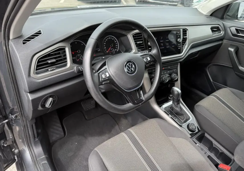 Vue intérieure côté conducteur du Volkswagen T-Roc gris Indium, volant cuir multifonction et console centrale avec écran tactile.