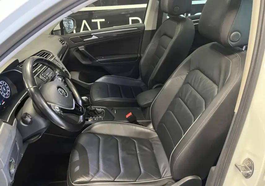 Vue intérieure côté conducteur du Volkswagen Tiguan 2017 avec sièges sport en cuir noir et tableau de bord digital.