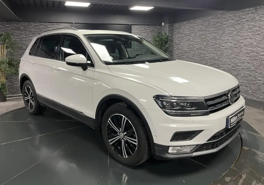Volkswagen Tiguan blanc en 3/4 avant droit, avec jantes alliage noires et phares LED dans un showroom.
