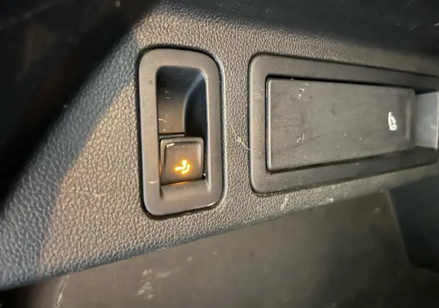 Gros plan sur le bouton de rabattement électrique du siège arrière dans l'habitacle du Volkswagen Tiguan blanc.