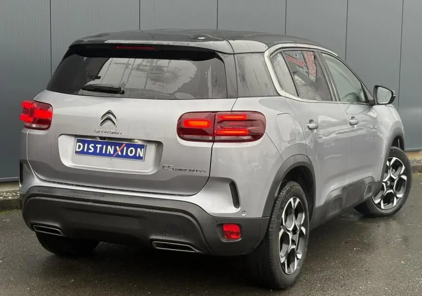 Vue 3/4 arrière droite d'un Citroën C5 Aircross Hybrid gris Artense avec toit noir et feux arrière LED allumés.