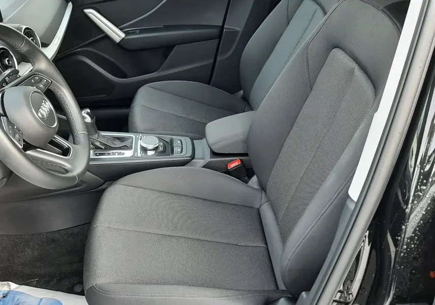 Vue intérieure côté conducteur de l'Audi Q2 2023 noir mito metal, sièges tissu gris et console centrale avec commandes.