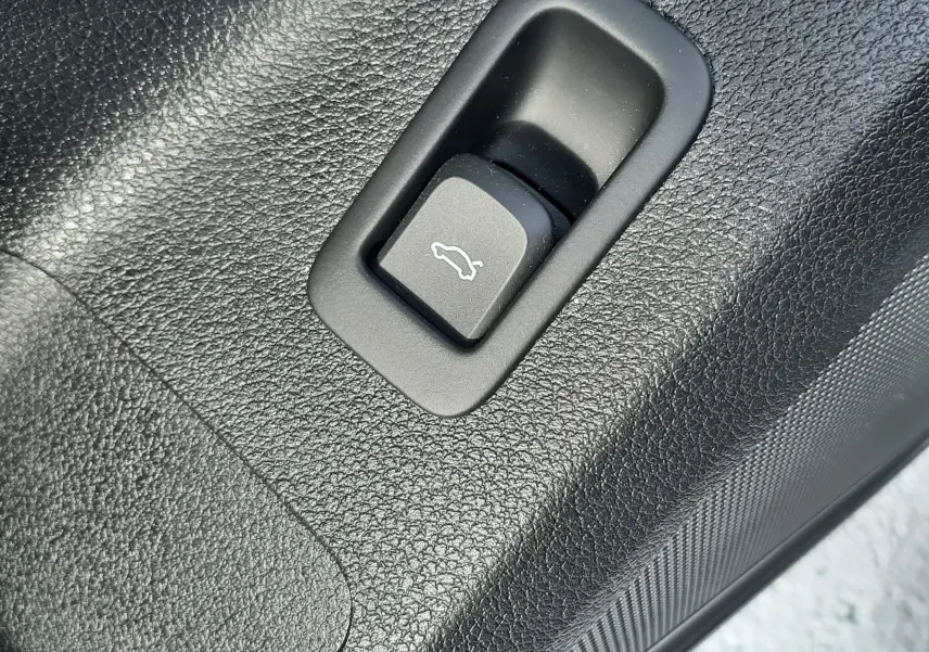Gros plan sur le bouton d'ouverture de coffre en plastique noir texturé à l'intérieur d'un Audi Q2 noir mito metal 2023.
