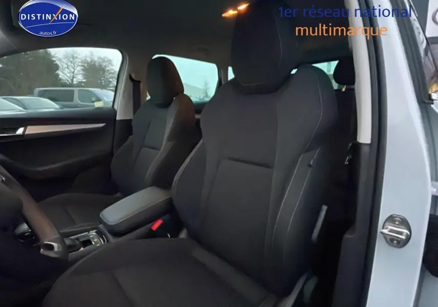 Vue intérieure côté avant droit du Skoda Karoq blanc glacial, mettant en valeur les sièges noirs et l'accoudoir central.