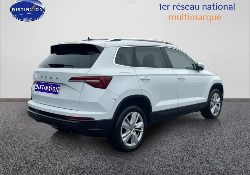 Vue 3/4 arrière droite d'un Skoda Karoq blanc glacial avec jantes alu et vitres arrière surteintées.