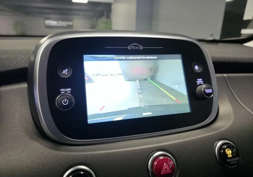 Écran central tactile de la Fiat 500X 2024 montrant la caméra de recul, avec tableau de bord gris et commandes autour.