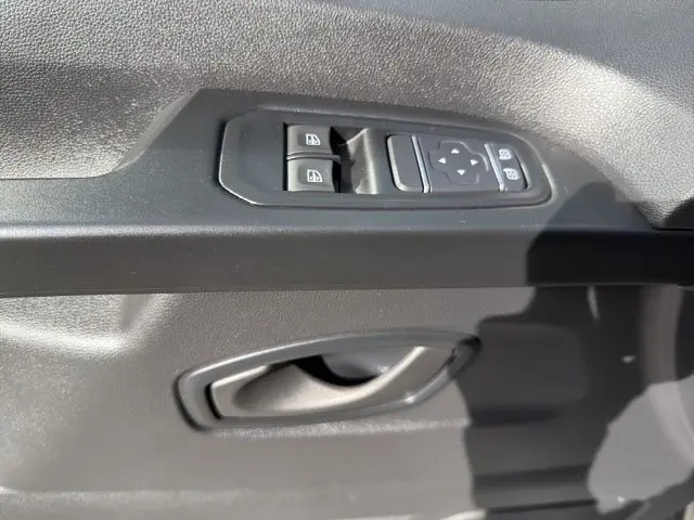 Gros plan sur la commande des vitres électriques et la poignée intérieure côté conducteur du Renault Trafic Fourgon gris clair.