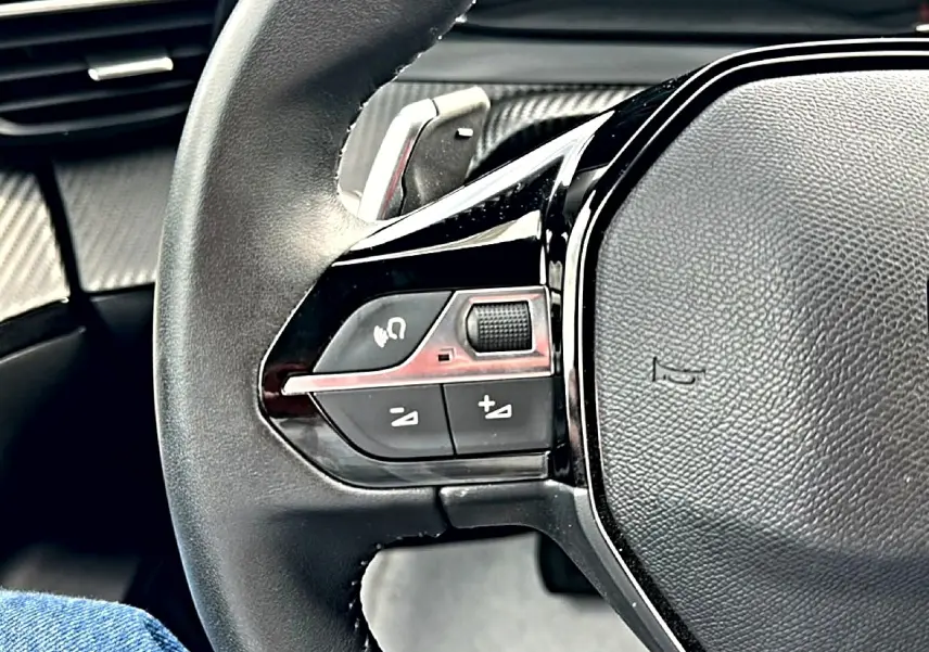 Gros plan sur le volant noir multifonction du Peugeot 2008 1.2 hybrid 145 style, avec commandes intégrées côté gauche.