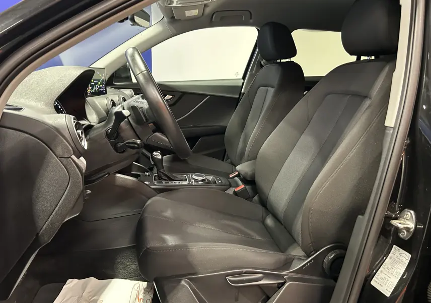 Intérieur noir de l'Audi Q2 35 TFSI 2023 vu côté conducteur, avec sièges tissu et tableau de bord moderne.