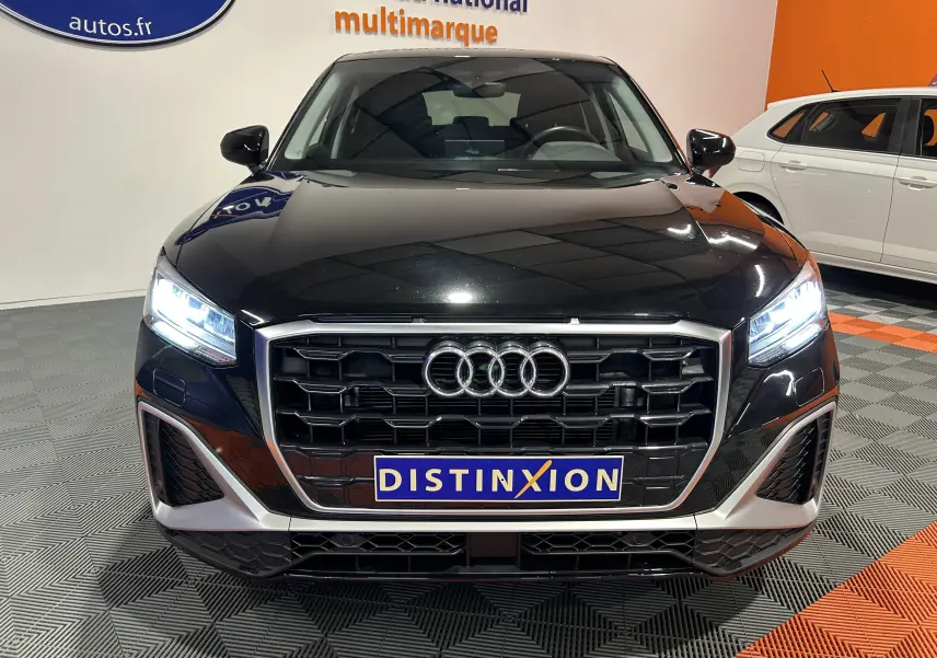 Audi Q2 noir métal vue de face avec calandre S-Line et phares LED allumés dans un showroom