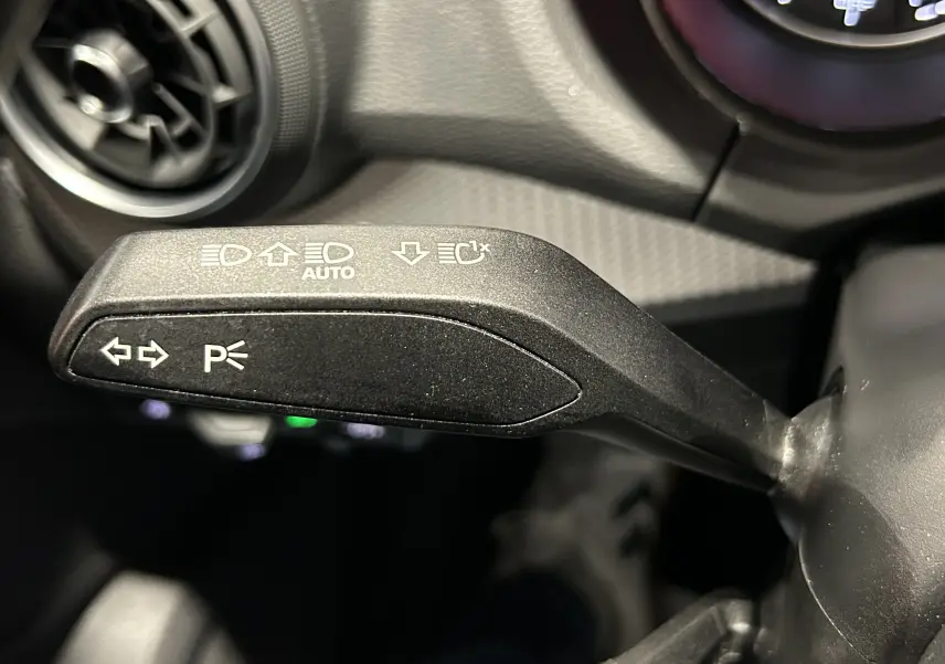 Gros plan sur le bouton de commande des phares avec réglage automatique, sur l'Audi Q2 noir métal 2023.