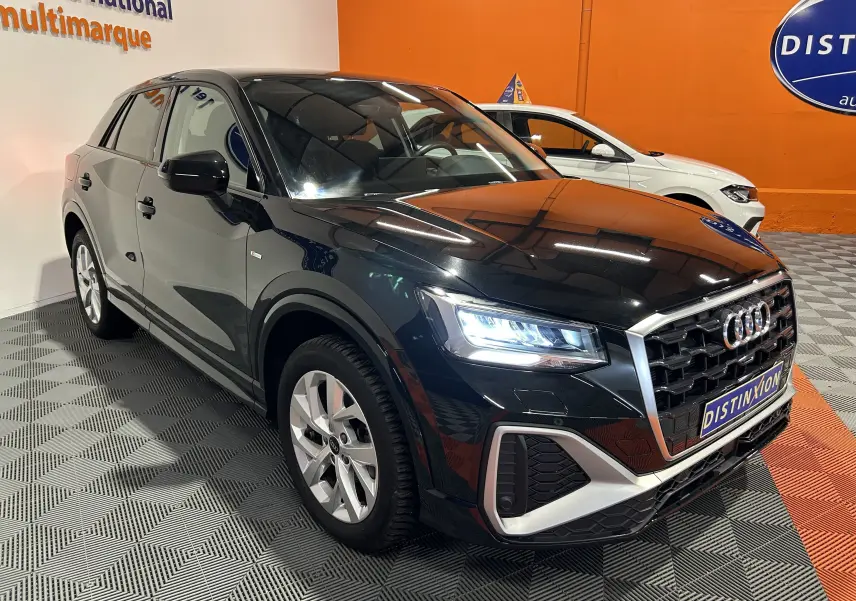Audi Q2 noir métal en 3/4 avant droit avec phares allumés et calandre S-Line dans un showroom.