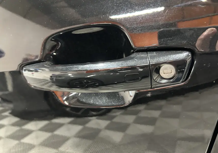 Gros plan sur la porte arrière droite noire métallisée de l'Audi Q2 35 TFSI 2023 avec reflet d'un mur orange.