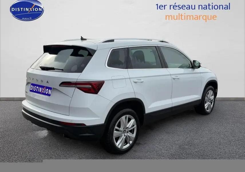 Vue 3/4 arrière droite d'un Skoda Karoq blanc glacial avec barres de toit et jantes alu.