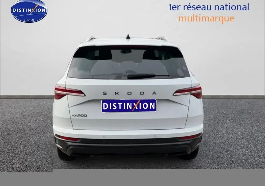 Vue arrière d'un Skoda Karoq blanc glacial avec feux arrière LED et barres de toit visibles.