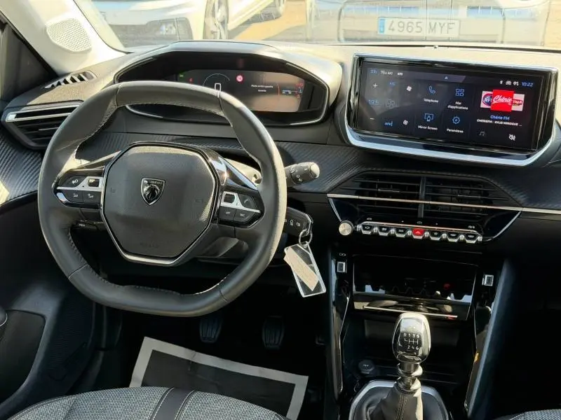 Vue intérieure centrée sur le volant et la console centrale de la Peugeot 208 1.2 100ch, avec écran tactile et levier de vitesses.