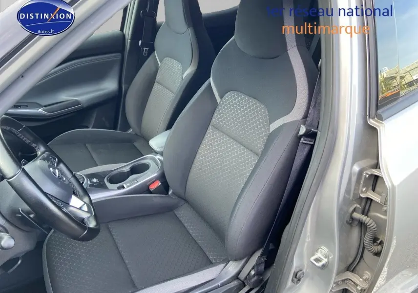 Vue intérieure côté conducteur du Nissan Juke gris clair 2021, mettant en valeur les sièges en tissu noir et la console centrale.