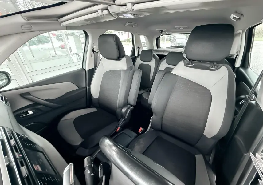 Vue intérieure avant droite du Citroën C4 Picasso 2015 avec sièges tissu noir et gris clair, toit ouvrant panoramique visible.