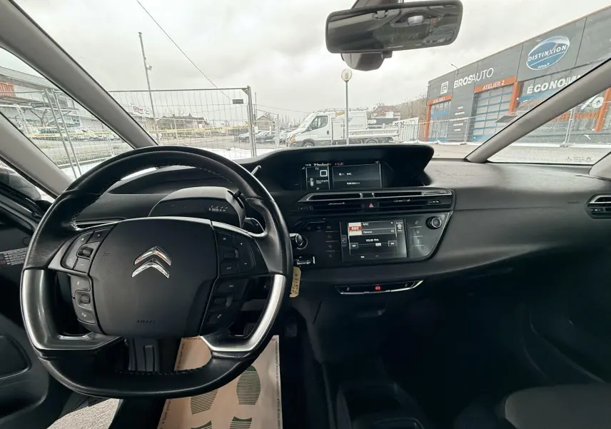 Vue intérieure centrée sur le volant et tableau de bord noir du Citroën C4 Picasso gris platinium, avec écran tactile et commandes au volant.