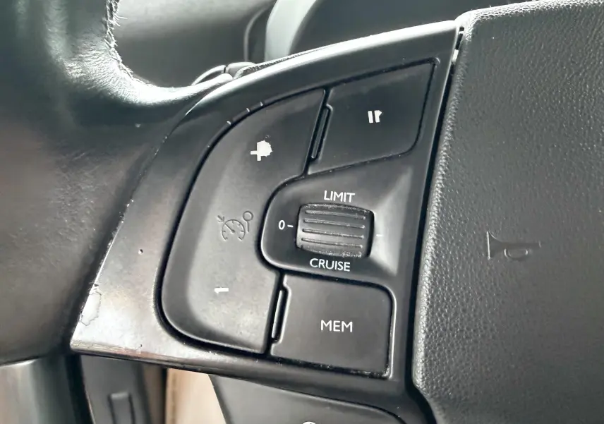 Gros plan sur les commandes de régulateur de vitesse au volant noir d'une Citroën C4 Picasso gris platinium.