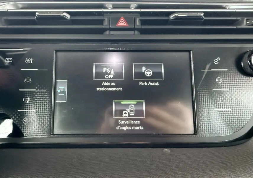 Vue rapprochée de l'écran tactile central du tableau de bord montrant les aides au stationnement et la surveillance d'angles morts.